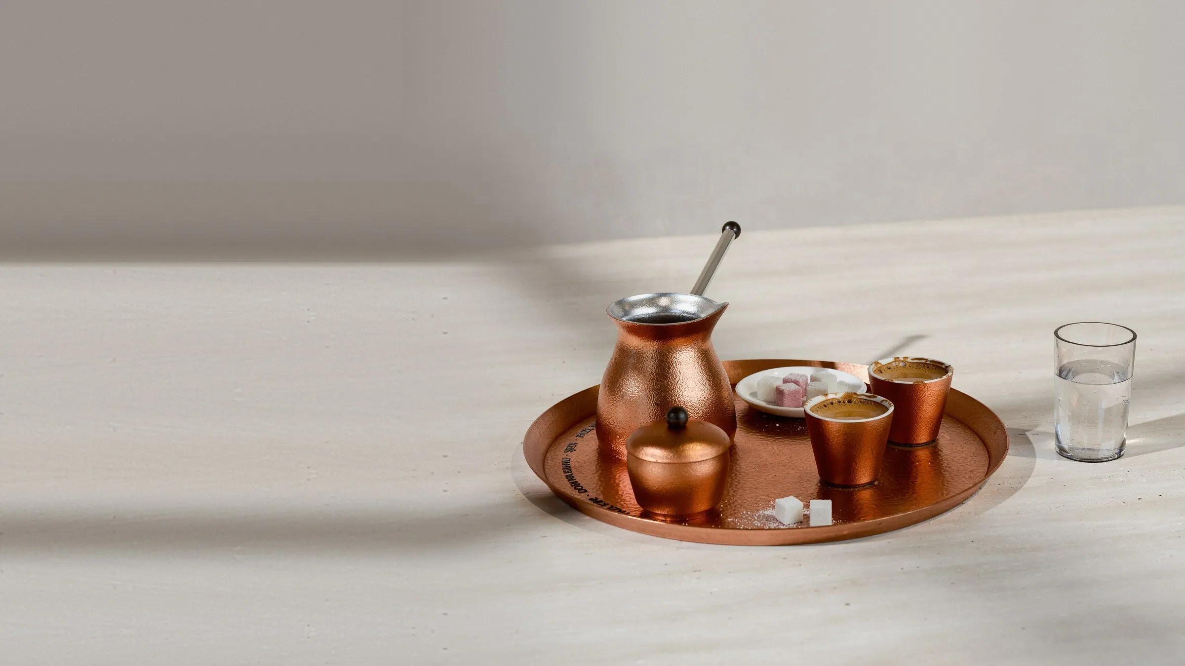 The Baščaršija edition in hammered copper: džezva, two fildžani of coffee, sugar bowl and rahat lokum on a copper tray, with a glass of water, in window light
