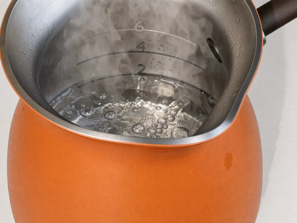 Inside the džezva: water at a rolling boil up to the line marked 2, with the 4 and 6 lines above it